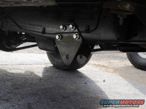 Close-up of a black metal bracket bolted to a vehicle's frame, near a tire