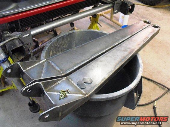 Two fabricated steel radius arms with mounting holes and hardware, resting on a large plastic bin