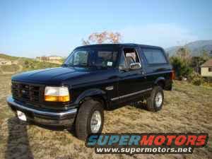 Black 1996 Ford Bronco parked on a grassy hill with houses and trees in the background
