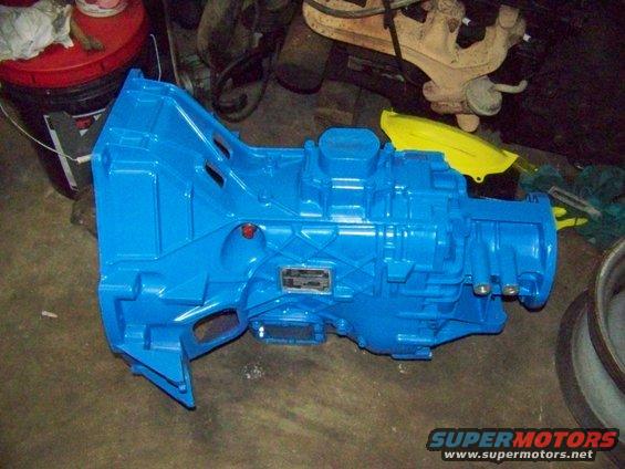 Blue transmission with a metal plate on its side, resting on a concrete floor
