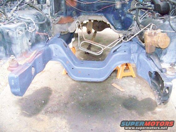 Vehicle frame with engine components and suspension parts visible, supported by jack stands
