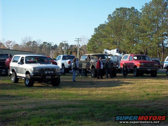 Several lifted SUVs and trucks parked on a grassy field under a clear sky