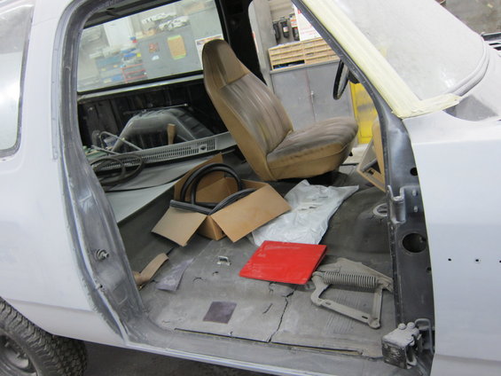 Interior of a pickup truck with open door, showing worn seat, floor, and parts