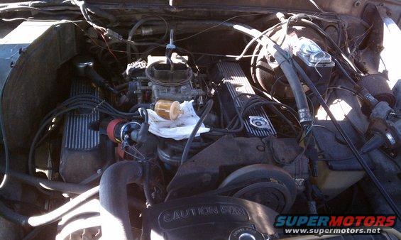 Engine bay with carburetor and V8 valve covers. Visible text: CAUTION FAN