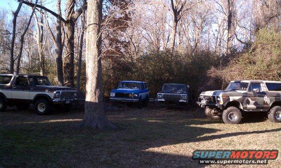 Four SUVs parked in a yard with trees. One is brown and white, two are blue and dark, and one is camo