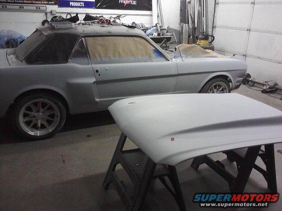 1966 Ford Mustang coupe in body shop, prepped for paint. Hood is off and on a stand