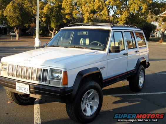 White 1994 Jeep Cherokee parked on asphalt, trees in background