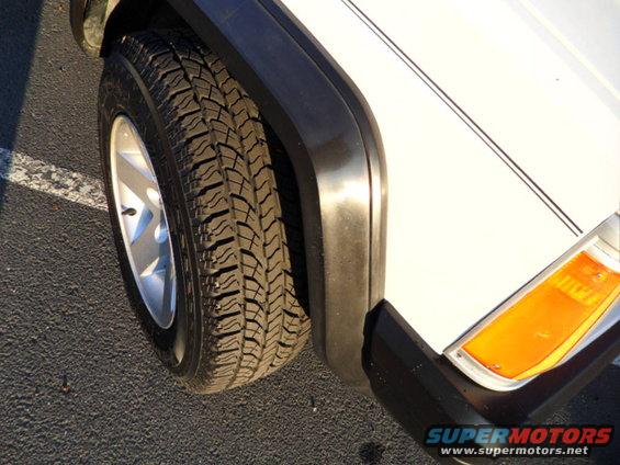 Front wheel and fender of a white Jeep Cherokee with a black fender flare and orange turn signal