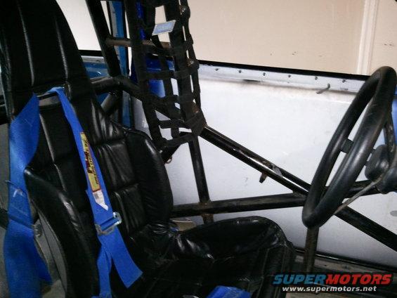Black racing seat with blue harness and roll cage structure inside a vehicle