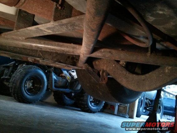 Underside view of a vehicle with multiple tires and suspension components visible. Another vehicle is partially seen in the background