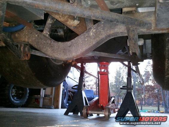 Undercarriage of a vehicle on jack stands, showing rusty suspension components and large tires