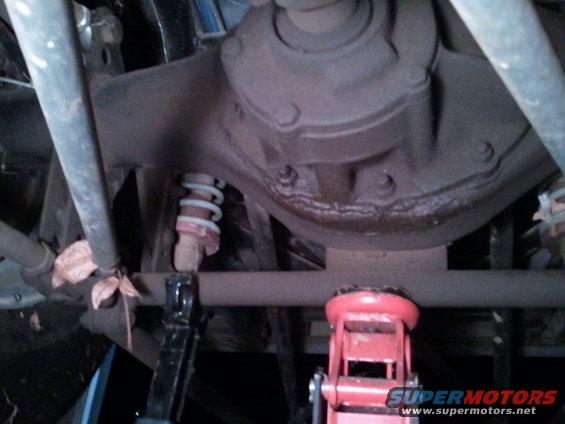 Underside of a vehicle showing the rear axle, differential, and suspension with a jack and jack stands