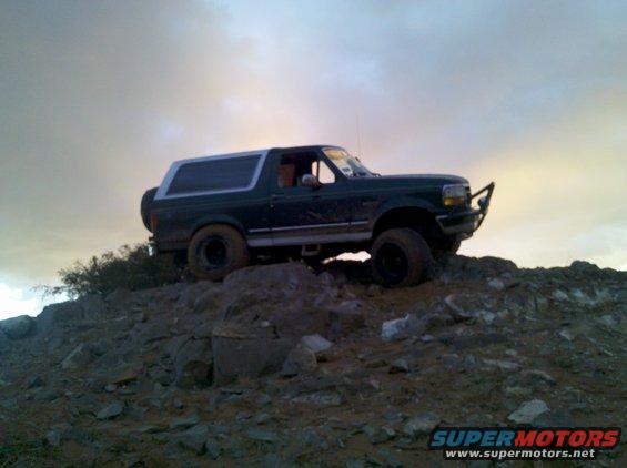 Dark green Ford Bronco on rocky terrain under a cloudy sky