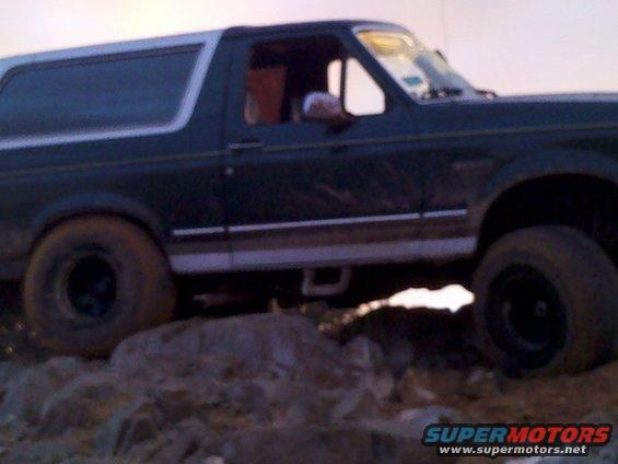 Dark green SUV with a white roof, off-roading over rocks. Visible side profile shows a two-door body style