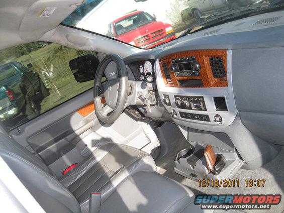 Gray leather seats and dashboard of a truck interior with wood trim and a red Dodge pickup visible through the windshield
