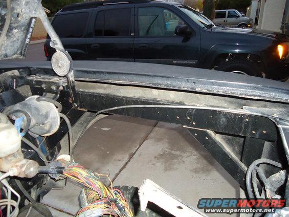 Close-up of a vehicle's engine bay with exposed wires. A dark SUV is parked behind it