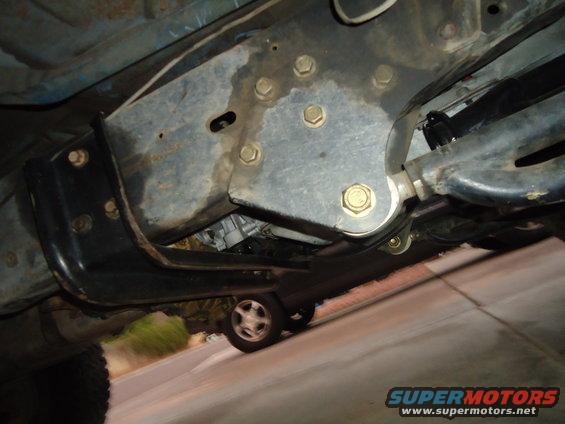 Underside of a truck frame with visible suspension components and a distant wheel
