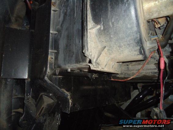 Close-up of engine bay with black plastic housing, red wire, and metal brackets. Dusty and dirty