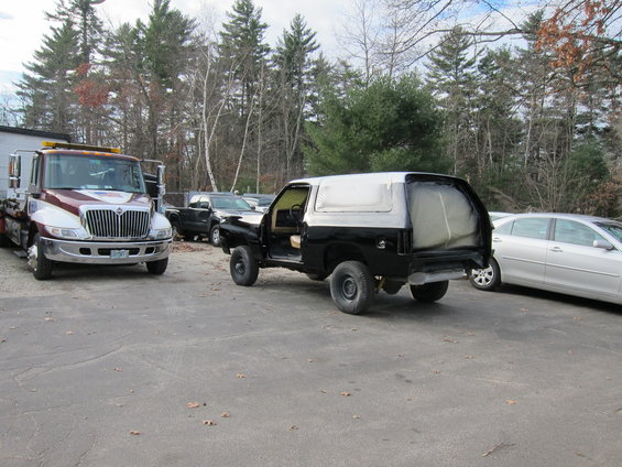 Black SUV in primer, rear view, with tow truck and sedan