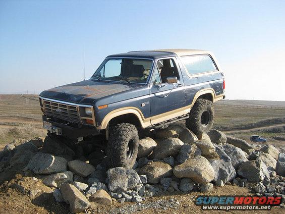 1985 Ford Bronco with lifted suspension and large tires climbing over a pile of rocks