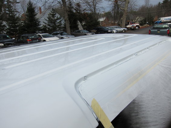 Close-up of a white pickup truck bed with ribbed sides, showing masking tape on the edge