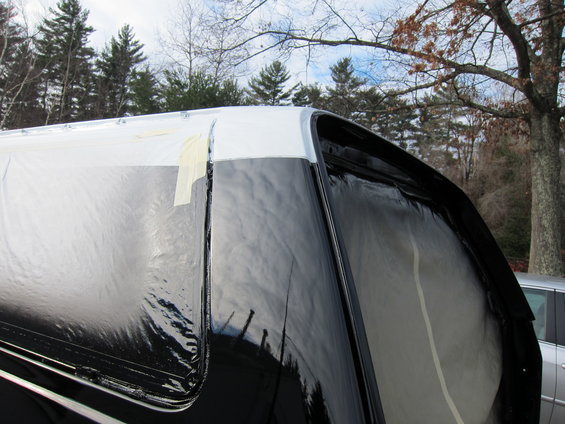 Top corner of a truck bed cap with black and white paint, covered in plastic and tape