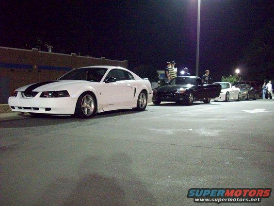 White 2000 Ford Mustang coupe with black hood stripes, parked at night