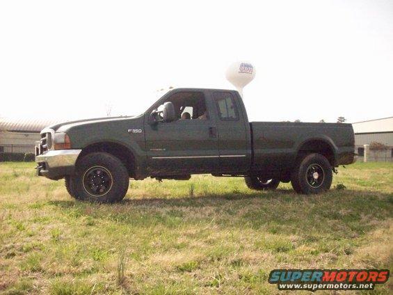 Green 2000 Ford F-350 pickup truck parked in a grassy field with a water tower in the background