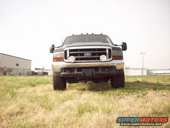 Dark gray Ford F-350 truck front view, parked on dry grass in front of industrial buildings