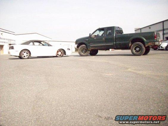 Green Ford F-350 truck parked next to a white Ford Mustang convertible