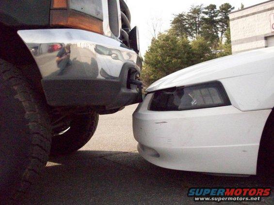 Front view of a white Ford Mustang bumper touching a chrome bumper of a dark-colored Ford F-350