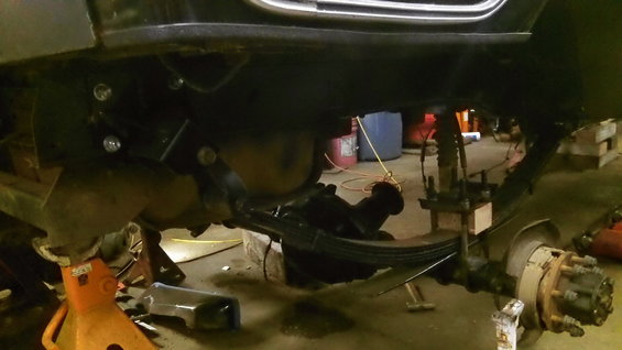 Underneath a vehicle, showing leaf springs, axle, and frame components. It's on jack stands