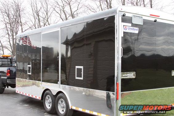 Black enclosed trailer with chrome trim, towed by a dark pickup truck with an orange light bar