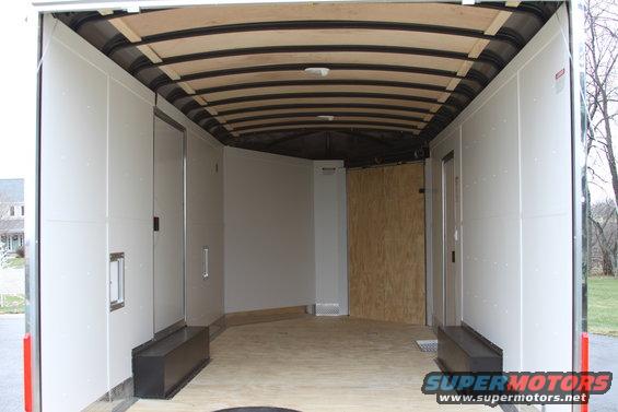 Interior view of an empty cargo trailer with white walls, wooden floor, and exposed ceiling beams