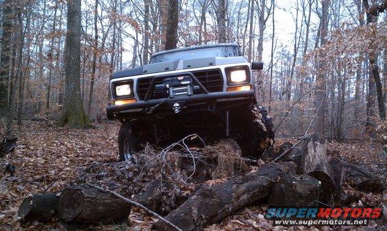 Ford Bronco with winch and custom bumper driving over logs in a forest