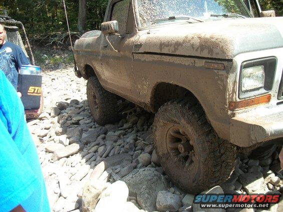 Mud-covered 1978 Ford Bronco navigating a rocky trail; another vehicle is partially visible to the left