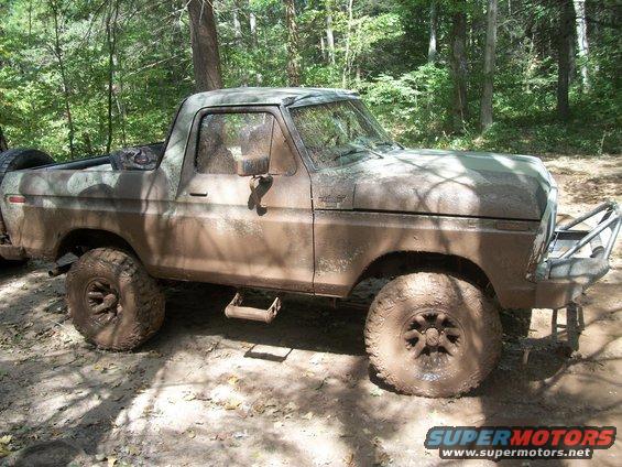 Muddy SUV with off-road tires and a custom bumper, parked in a wooded area