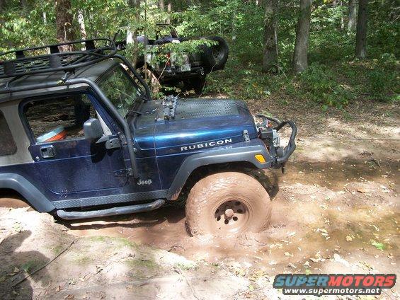 Blue Jeep Wrangler Rubicon stuck in mud with another Jeep visible in background trees