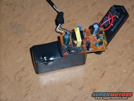 Electronic circuit board with yellow transformer, capacitors, and red LED, connected to a black power adapter housing and wires