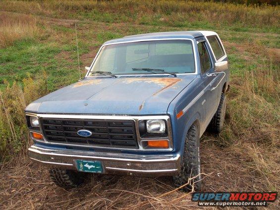 1985 Ford Bronco parked in a grassy field, hood shows rust spots