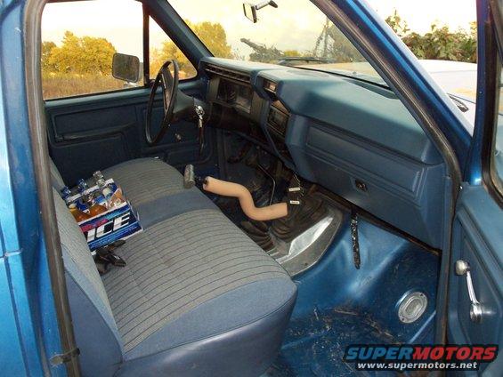 Blue truck interior with striped seats, dashboard, and steering wheel. A pack of ICE beer is on the passenger seat