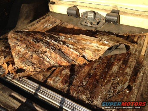 Rusted interior floor pan with exposed metal ribs and seatbelt anchors