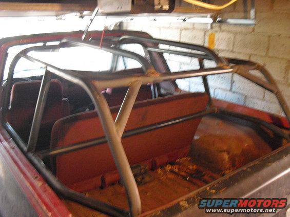 Red 1980s Ford Bronco interior with aftermarket roll cage, orange seats, and debris on the floor