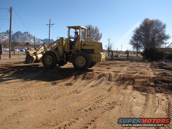 Yellow Fiat-Allis front loader tractor operating on a dirt lot with mountains in the background