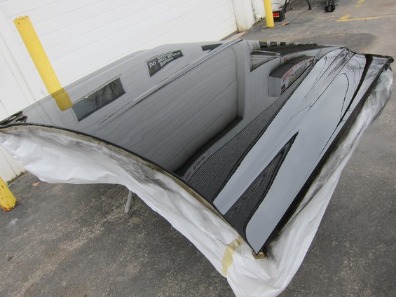Black car hood covered in protective plastic, reflecting a building