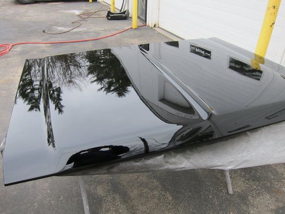 Black car hood resting on sawhorses, reflecting trees and a building