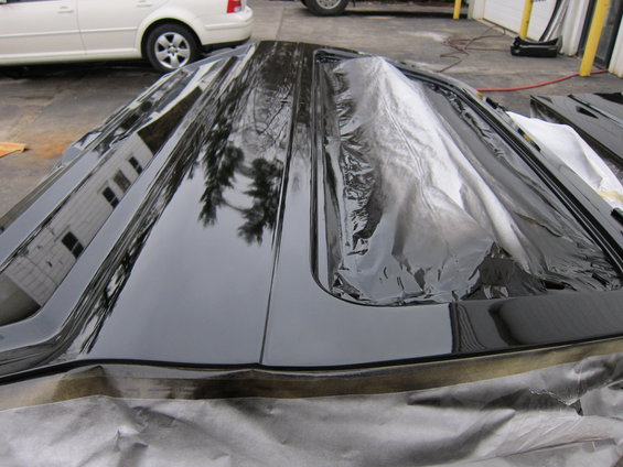 Black car roof panel with plastic sheeting on it, parked outside next to a white car