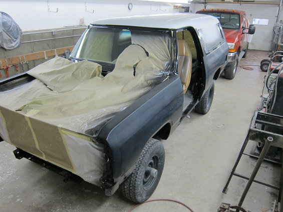 Black and silver SUV in a garage, covered in masking paper and plastic, with its doors open