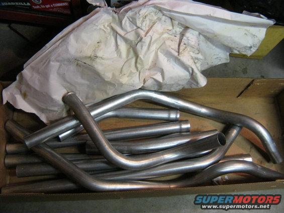 Box of bent metal exhaust pipes, some covered in crumpled paper