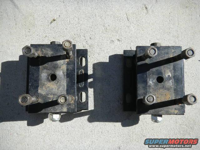 Two black engine mounts with bolts and nuts on a concrete surface